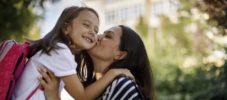 Mother kissing daughter in front of school