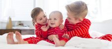 USA, Utah, Salt Lake City, Boy (6-7) and girl (4-5) embracing brother (2-3) on bed
