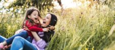 Happy mother and her small daughter lying down on the grass in spring nature, laughing.