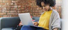 Woman writing in diary while using laptop computer on sofa