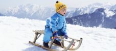 Germany, Tegernsee, Wallberg, smiling little boy sitting on sledge