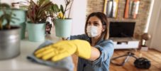 Woman wiping dust from shelf and other furniture in living room