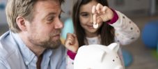 Daughter putting coin in piggy bank held by father at home