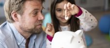 Daughter putting coin in piggy bank held by father at home