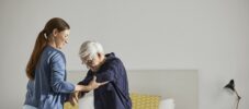 Female caregiver supporting senior man in standing